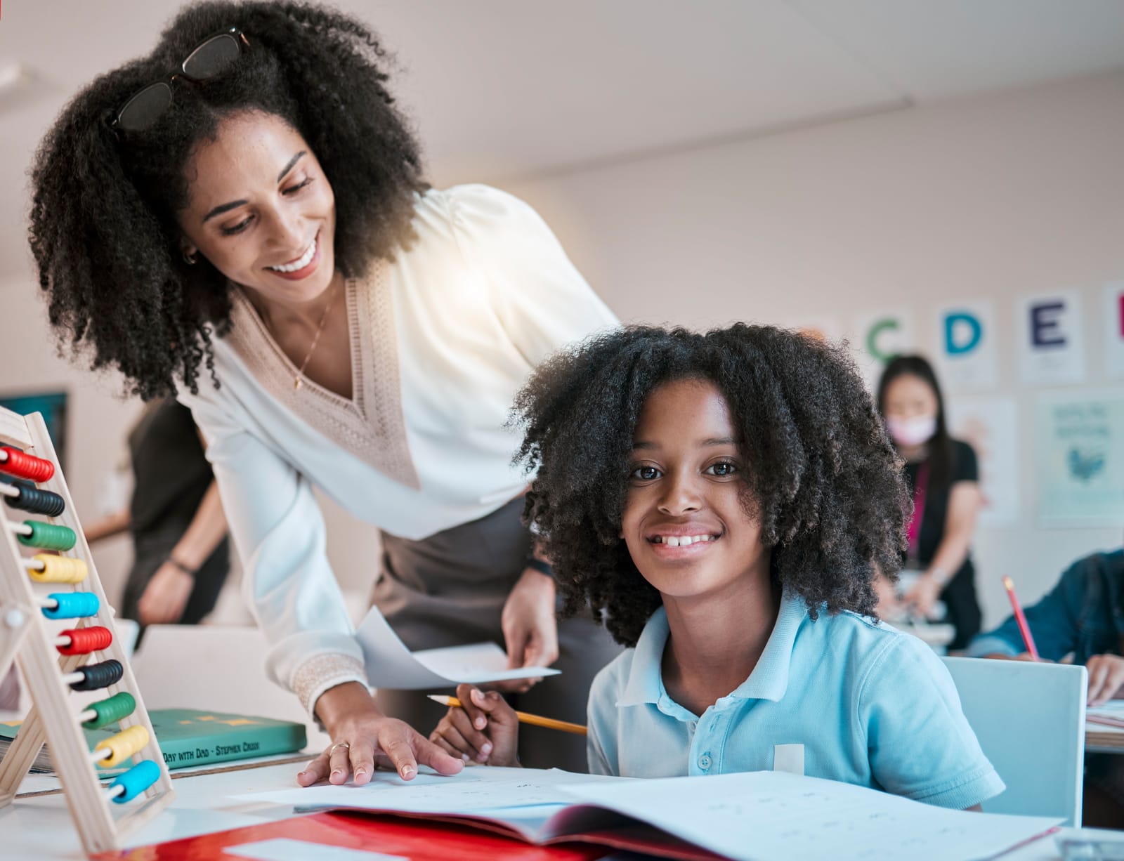 52545522_young-child-learning-maths-happy-teacher-in-classroom-with-children-and-knowledge-at-desk-female-educator-writing-in-workbook-reading-kids-notebook-at-school-and-teaching-student-with-assignment